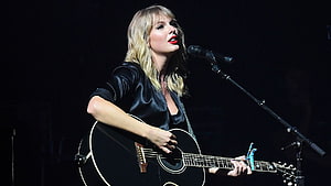 Taylor Swift performing live on stage with acoustic guitar and microphone HD wallpaper