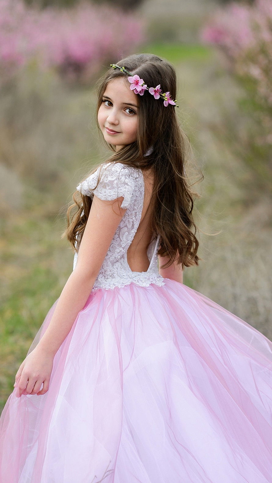 Young girl in a pink tulle dress with a floral hair accessory standing in a spring garden HD phone wallpaper