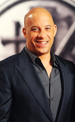 Vin Diesel smiling in a dark suit and grey shirt at a red carpet event HD phone wallpaper