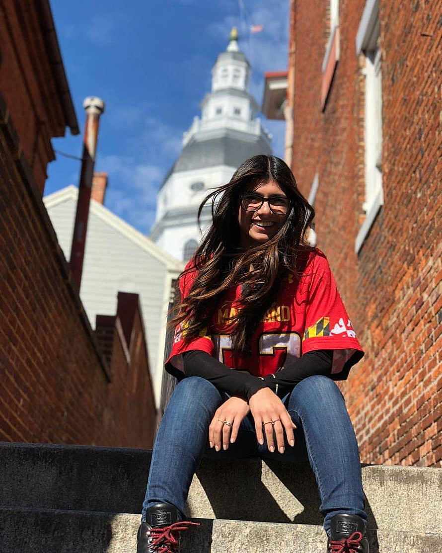Young woman in red Maryland jersey sitting on stone steps with historic church steeple in background HD phone wallpaper