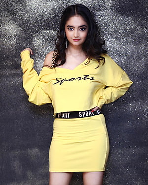 Anushka Sen in a yellow off-shoulder sport dress with leopard strap against a glittery backdrop HD phone wallpaper