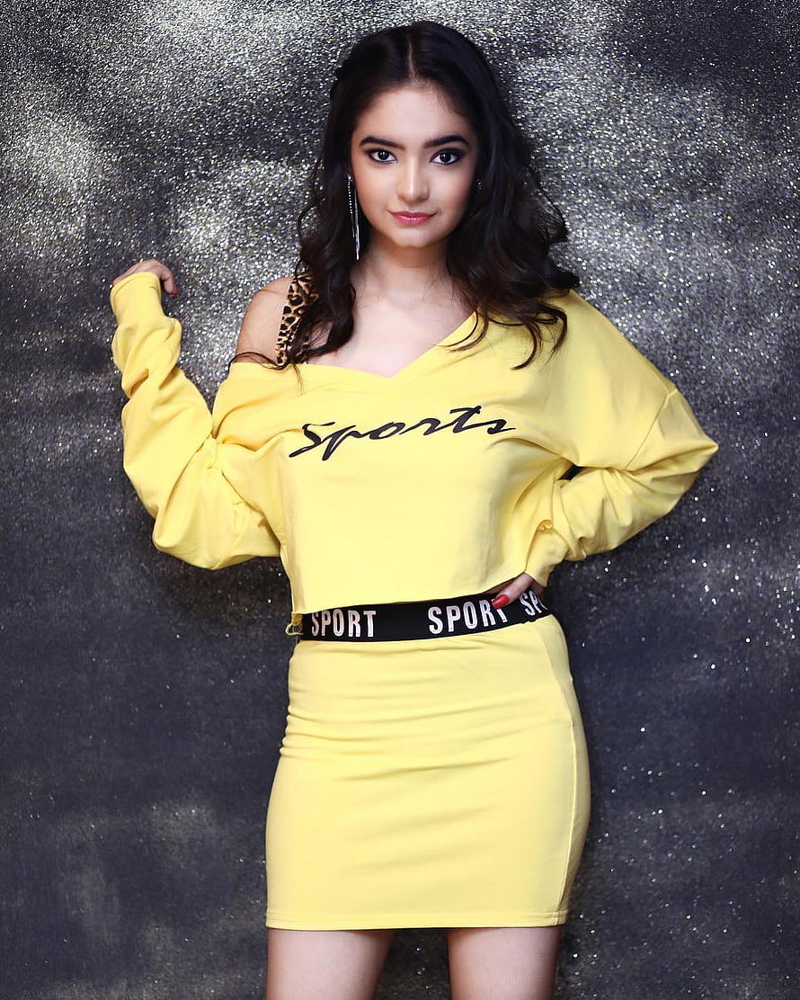 Anushka Sen in a yellow off-shoulder sport dress with leopard strap against a glittery backdrop HD phone wallpaper