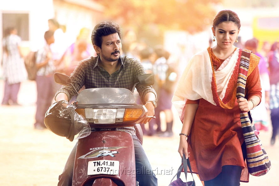 Manithan Movie Still: Man on Scooter and Woman in Traditional Attire Walking Through a Crowded Street HD wallpaper