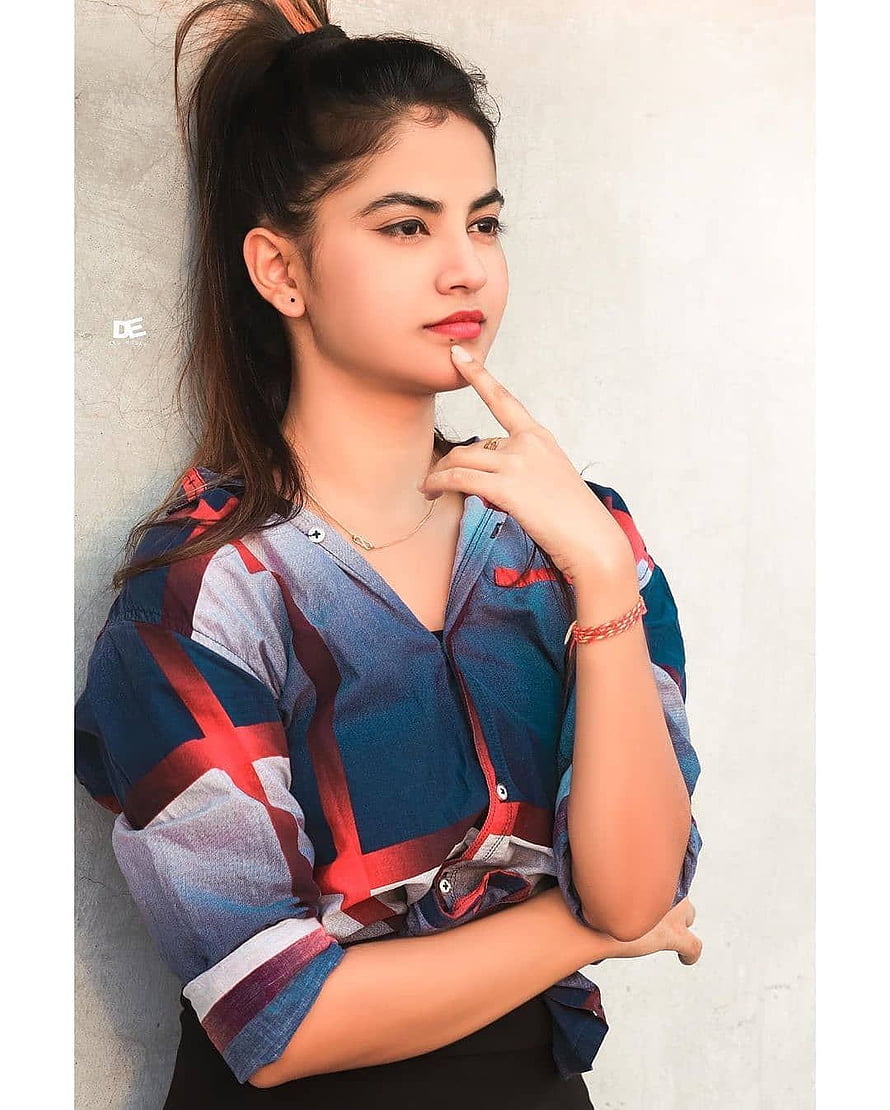 Priyanka Mongia in a colorful plaid shirt with a high ponytail against a white wall HD phone wallpaper