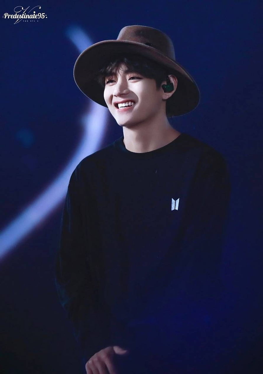 BTS V smiling on stage wearing a brown fedora hat and black long-sleeve shirt under blue concert lighting HD phone wallpaper