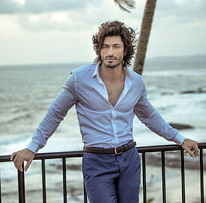 Vidyut Jammwal in a light blue shirt and navy trousers leaning on a seaside railing HD wallpaper