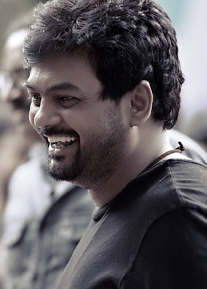 Puri Jagannadh smiling in profile wearing a black t-shirt with a blurred background HD phone wallpaper