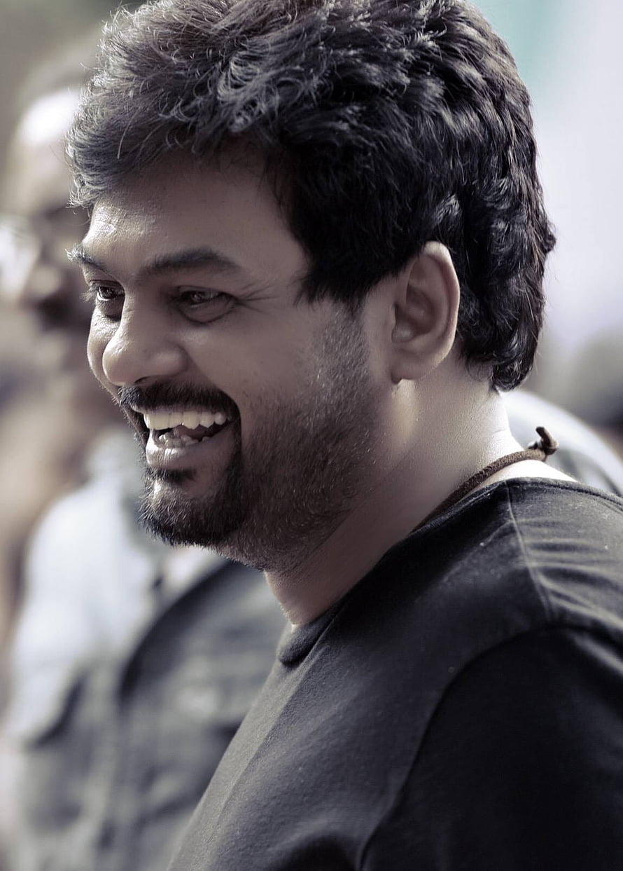 Puri Jagannadh smiling in profile wearing a black t-shirt with a blurred background HD phone wallpaper