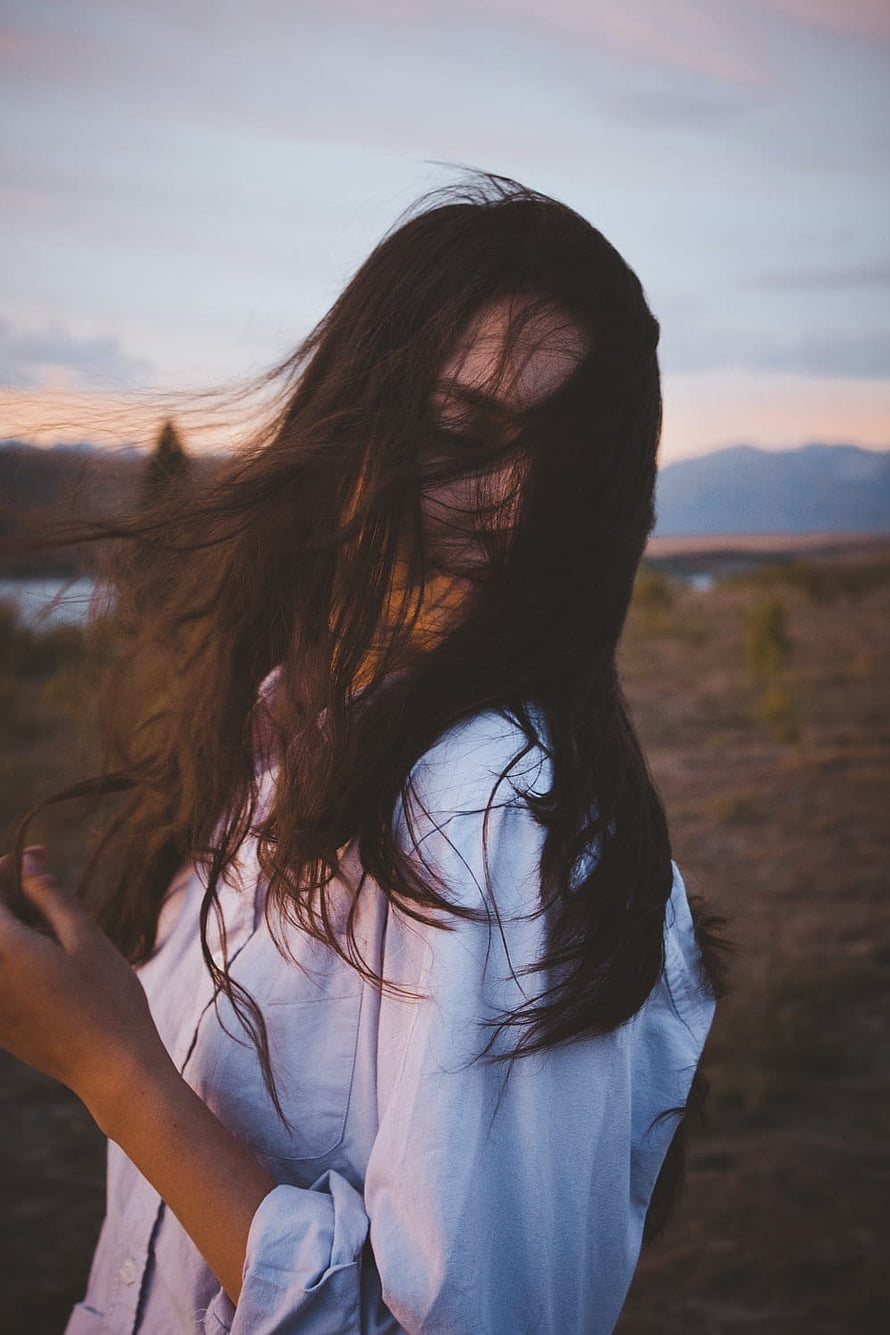 Woman with windblown hair covering face in a white shirt at sunset HD phone wallpaper