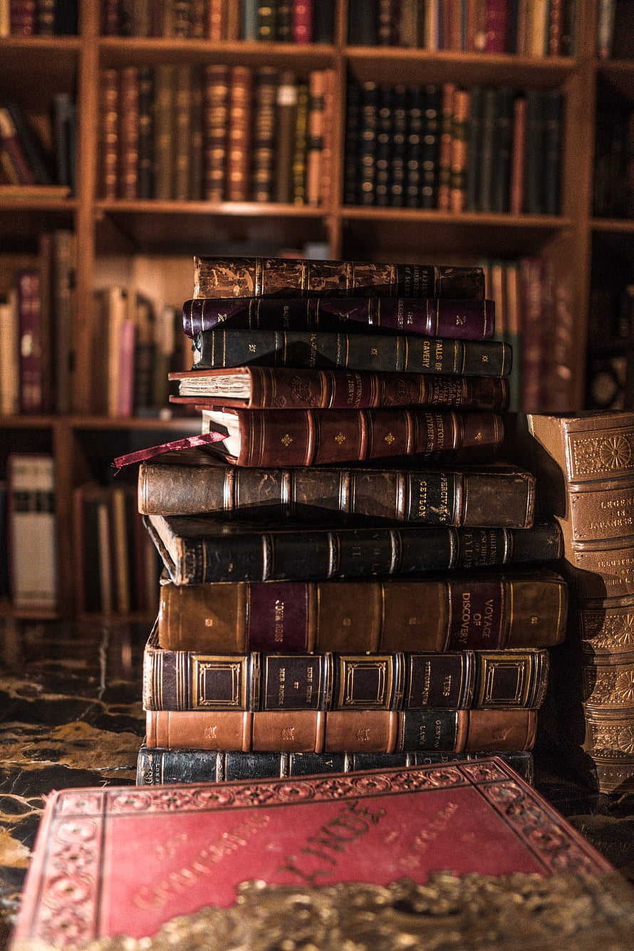 Stack of antique leather-bound books in a classic library setting HD phone wallpaper