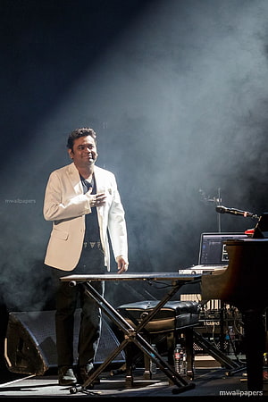 A R Rahman performing on stage in a white suit with dramatic lighting and smoke effects HD phone wallpaper