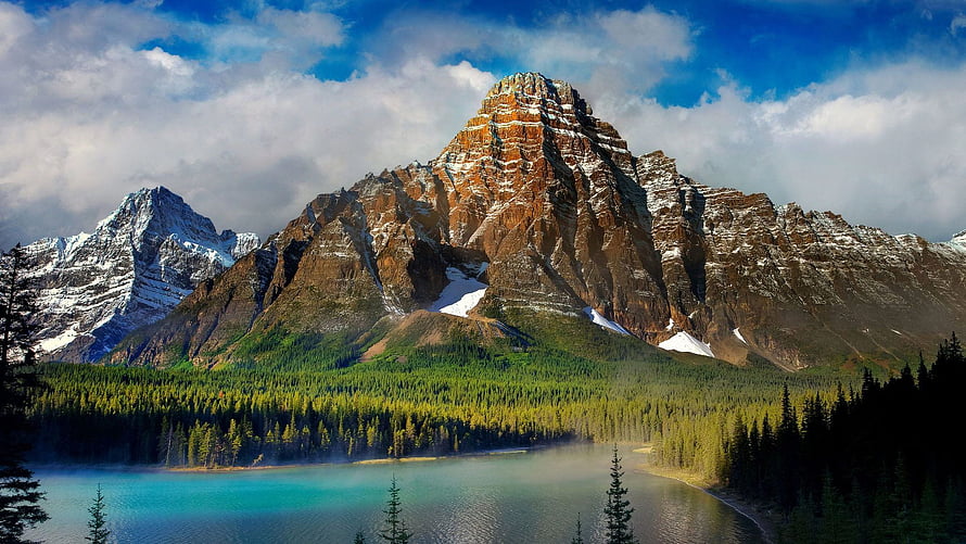 Majestic mountain peak rising above a turquoise alpine lake surrounded by dense evergreen forest HD wallpaper