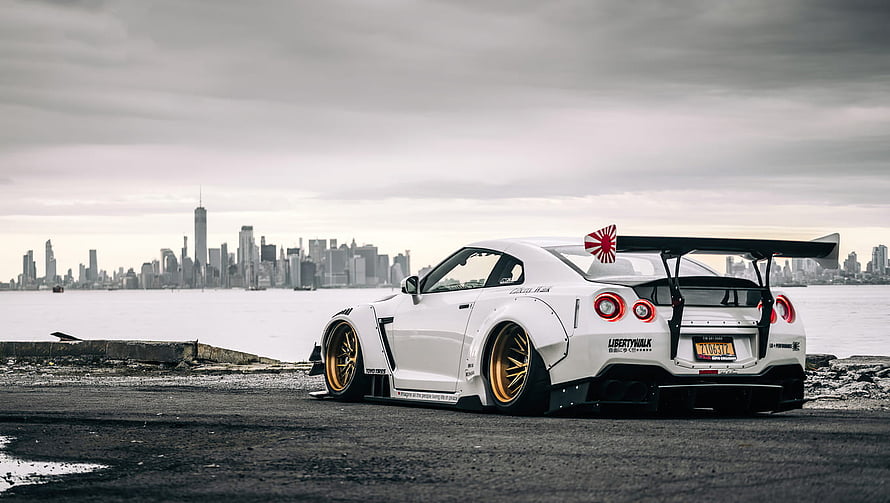 White Nissan GT-R with gold wheels parked on waterfront with New York City skyline in background HD wallpaper