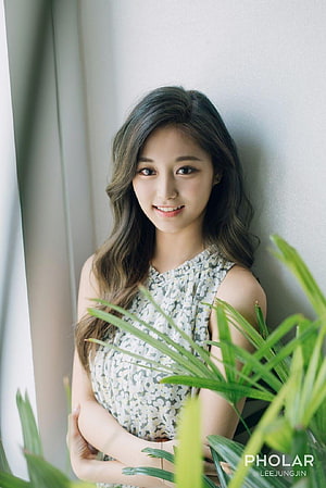 Tzuyu from TWICE in a floral dress posing beside green palm leaves in soft natural light HD phone wallpaper