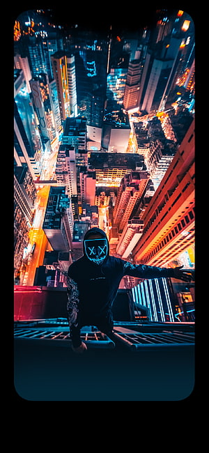 Person in glowing LED mask on rooftop overlooking neon-lit city skyline at night HD phone wallpaper