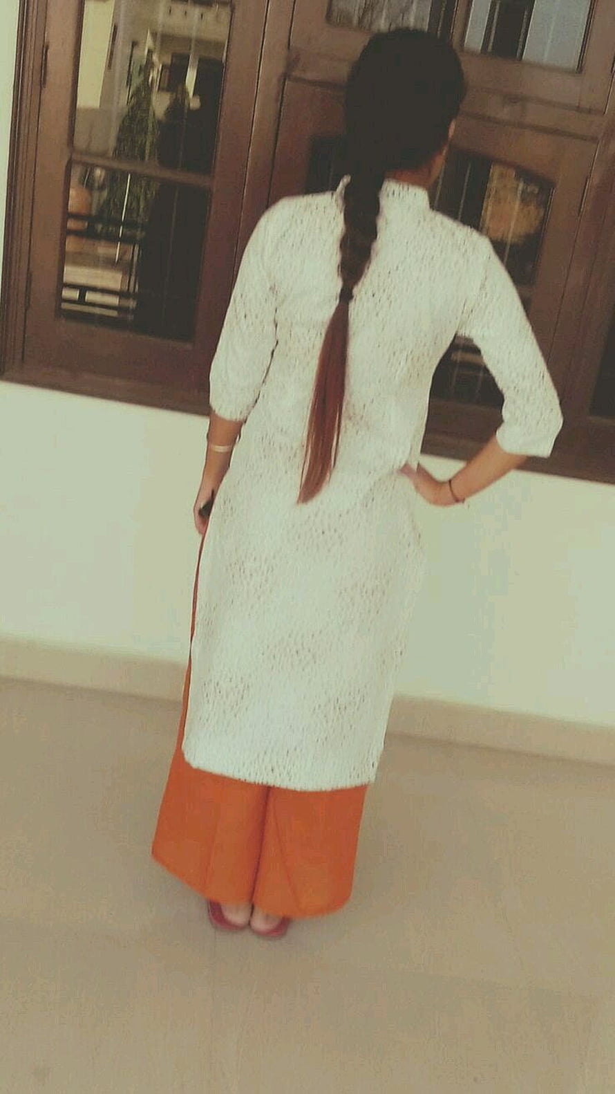 Woman in white lace tunic and orange palazzo pants standing by wooden window HD phone wallpaper
