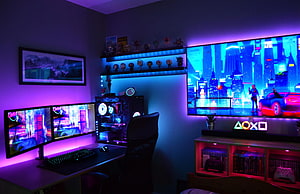 Neon-lit gaming room with dual monitors, RGB PC build, and large TV displaying a cyberpunk cityscape HD wallpaper