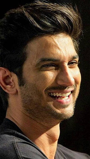Sushant Singh Rajput smiling portrait with short dark hair and stubble against a black background HD phone wallpaper