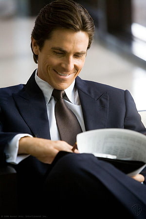 Christian Bale as Bruce Wayne in a navy suit reading a newspaper HD phone wallpaper