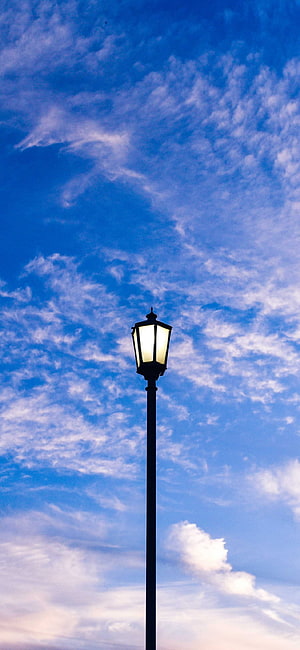 Vintage street lamp glowing against a vast blue sky with wispy clouds HD phone wallpaper
