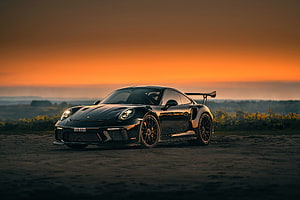 Black Porsche 911 GT3 RS with rear wing parked on dirt road at sunset HD wallpaper
