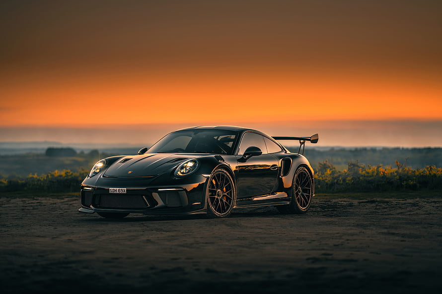 Black Porsche 911 GT3 RS with rear wing parked on dirt road at sunset HD wallpaper