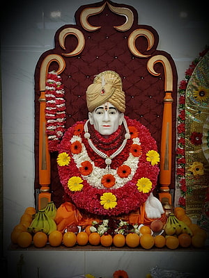 Shri Gajanan Maharaj adorned in vibrant floral garlands and fruit offerings on an ornate throne HD phone wallpaper