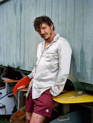 Pedro Pascal in Silk Shirt and Board Shorts Leaning Against Surfboards HD phone wallpaper