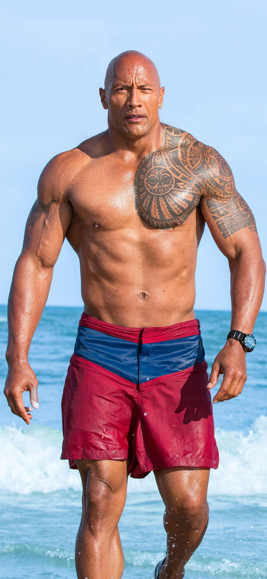 Dwayne Johnson shirtless on the beach in red swim trunks with ocean waves behind him HD phone wallpaper