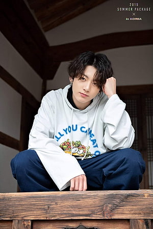 Jeon Jungkook in White Graphic Hoodie and Dark Trousers Seated on Wooden Bench HD phone wallpaper