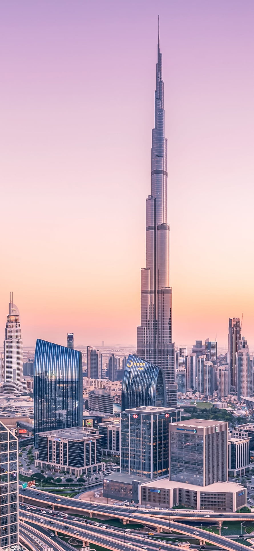 Burj Khalifa Tower Rising Over Dubai Cityscape at Sunset with Highway Interchange HD phone wallpaper