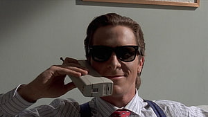Patrick Bateman in American Psycho holding a vintage brick phone with dark sunglasses HD wallpaper