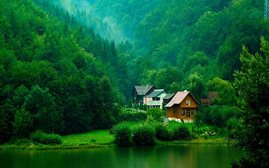 Secluded wooden cabins nestled in a lush green forest valley beside a calm lake HD wallpaper