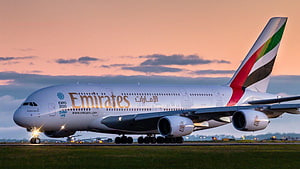 Emirates Airbus A380 on the runway at sunset with warm golden sky and landing lights glowing HD wallpaper