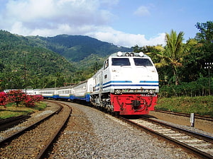 Indonesian passenger train traveling through lush tropical mountain landscape HD wallpaper