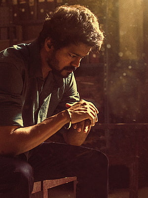 Vijay in a contemplative moment from the film Master, seated in warm cinematic lighting HD phone wallpaper