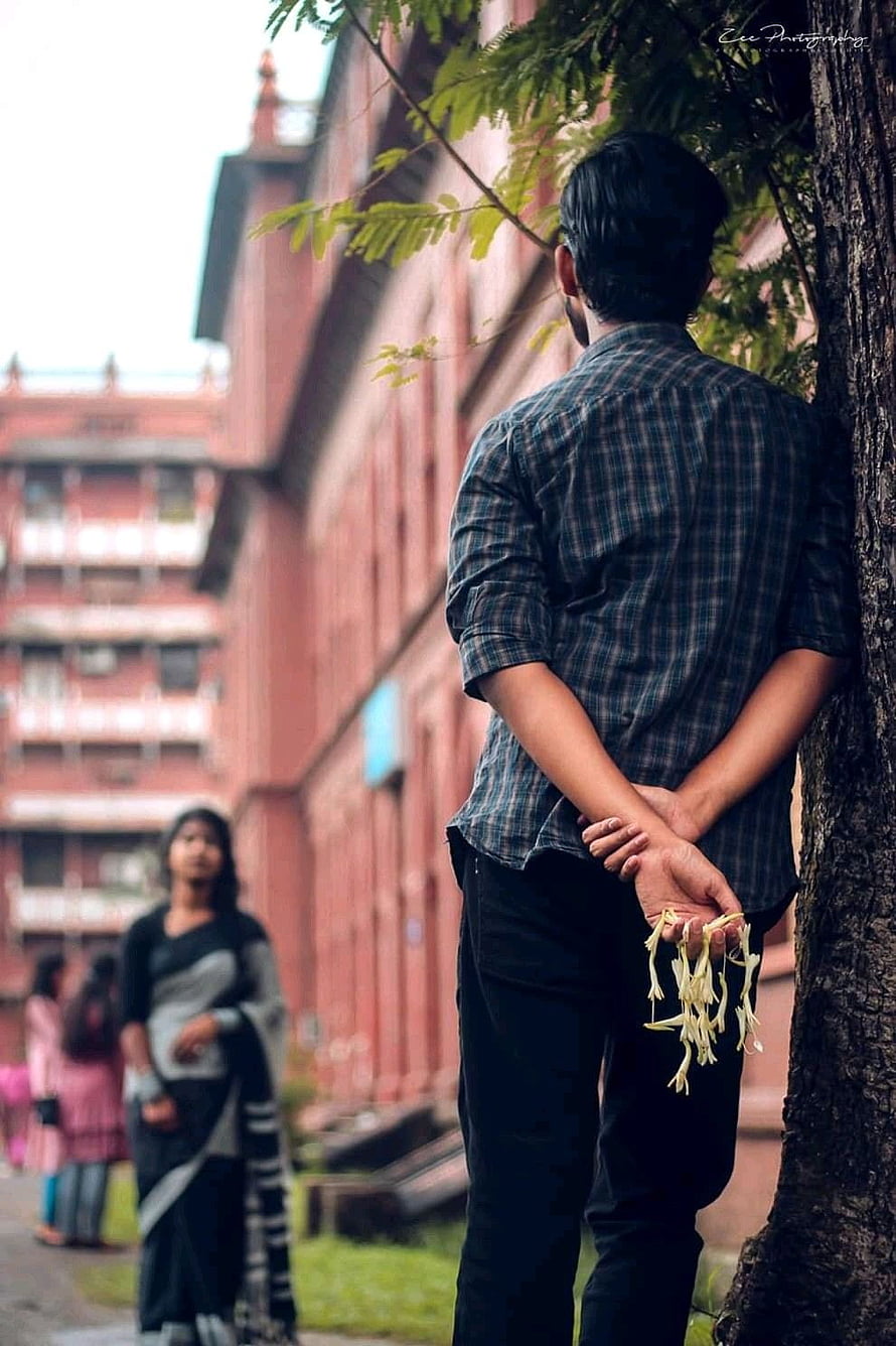 Man Leaning Against Tree Holding Flowers in Front of Red Brick Building, Pin on Bengali famous couple, bengali couples HD phone wallpaper