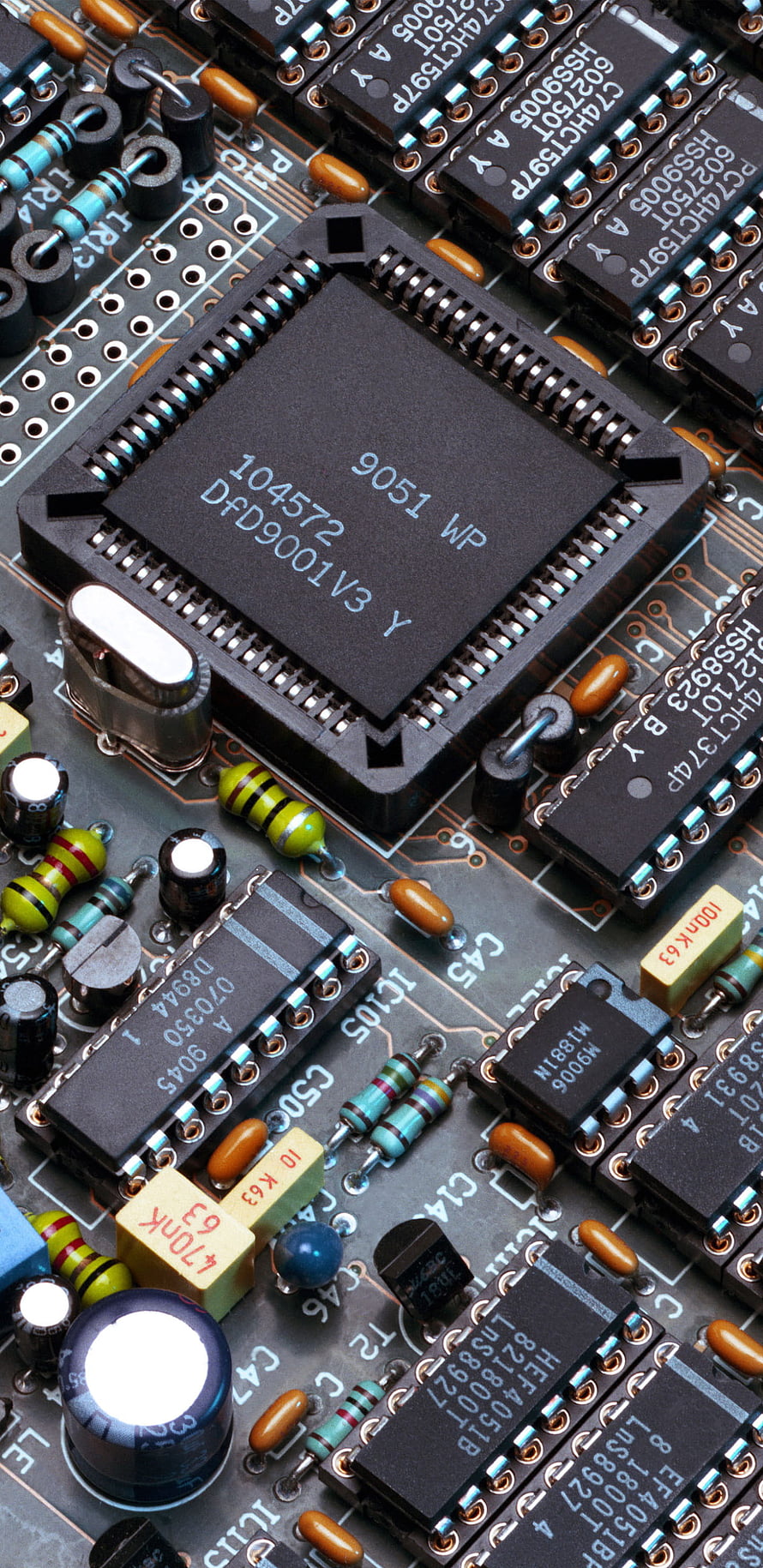 Close-up of a printed circuit board featuring a central microprocessor chip, capacitors, resistors, and integrated circuits HD phone wallpaper