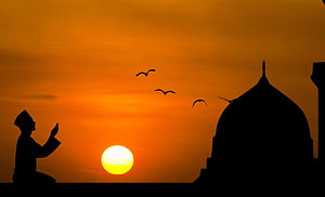 Silhouette of a Muslim man in prayer at sunset with mosque dome and birds in the sky HD wallpaper