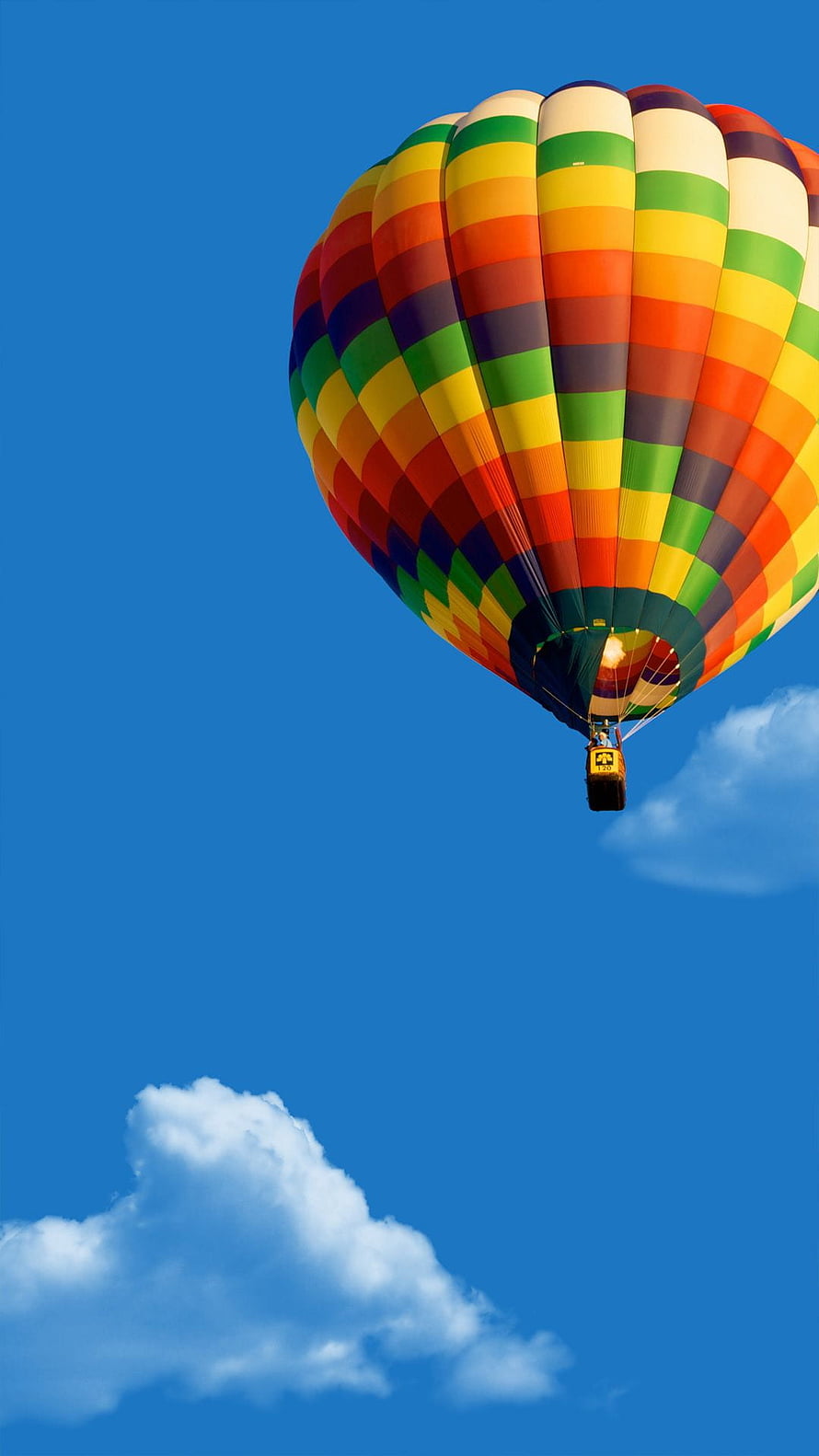 Vibrant multicolored hot air balloon soaring through a clear blue sky with scattered clouds HD phone wallpaper