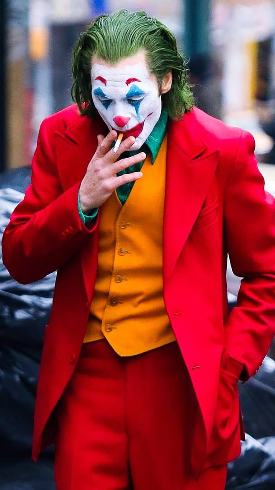 Joker in red suit smoking a cigarette with clown makeup and green hair HD phone wallpaper