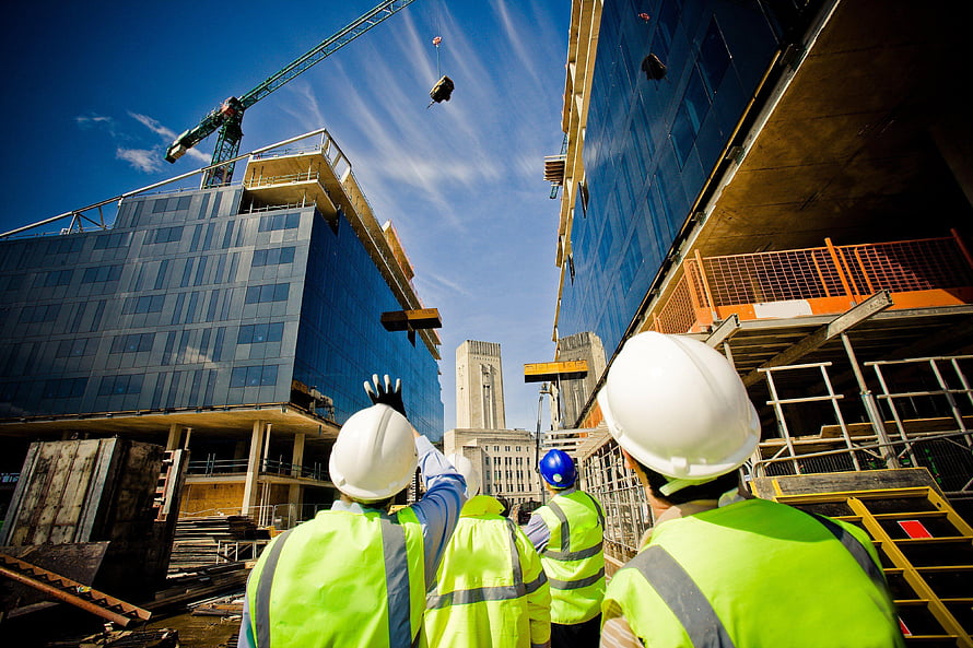 Construction workers in high-visibility vests and hard hats observing a crane lift materials at a modern building site HD wallpaper