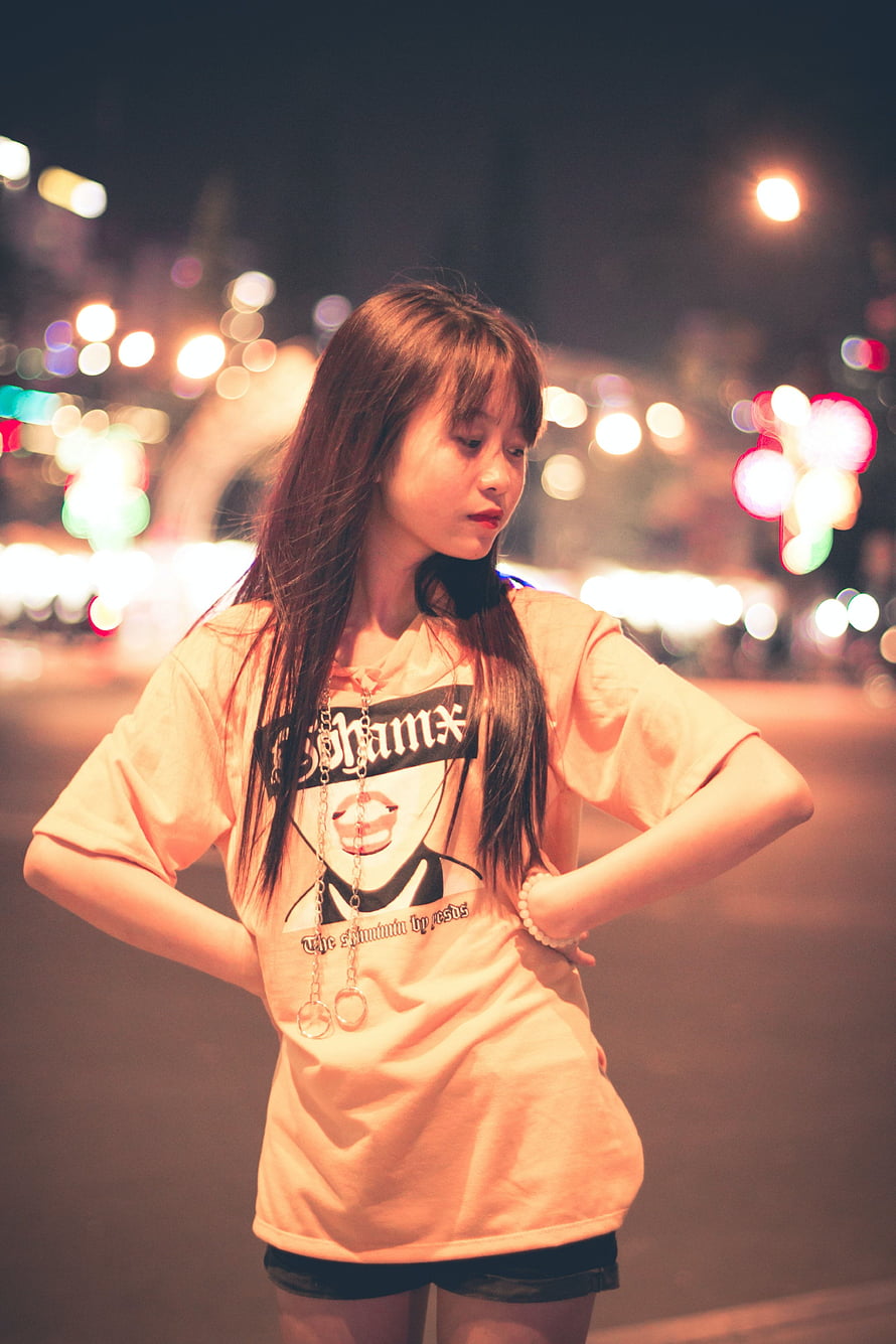 Young woman in graphic t-shirt posing on a city street at night with bokeh lights HD phone wallpaper