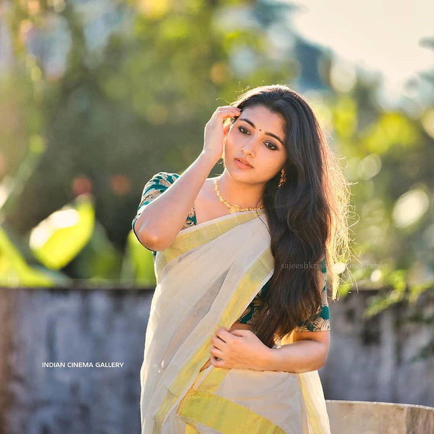 Mirna Menon in a cream and green sari with golden jewelry in a sunlit outdoor setting HD phone wallpaper