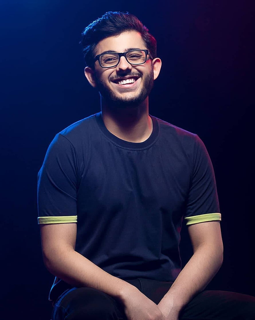 CarryMinati smiling portrait with glasses and dark t-shirt against a moody blue and red studio backdrop HD phone wallpaper