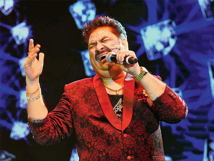 Kumar Sanu performing live on stage in a red patterned suit with microphone HD wallpaper