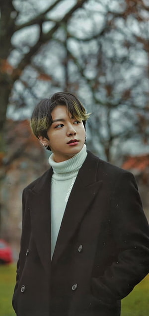 Jungkook in a black coat and white turtleneck with a blurred tree background HD phone wallpaper