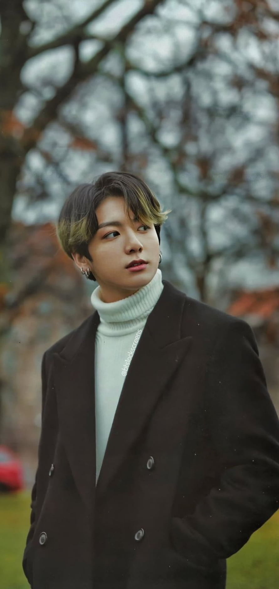 Jungkook in a black coat and white turtleneck with a blurred tree background HD phone wallpaper