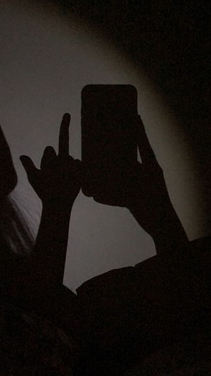 Silhouette of hands making a rude gesture while holding a smartphone in low light HD phone wallpaper