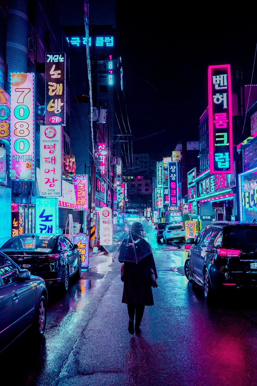 Lone figure with umbrella walking through rain-soaked Seoul street under vibrant neon signs at night HD phone wallpaper